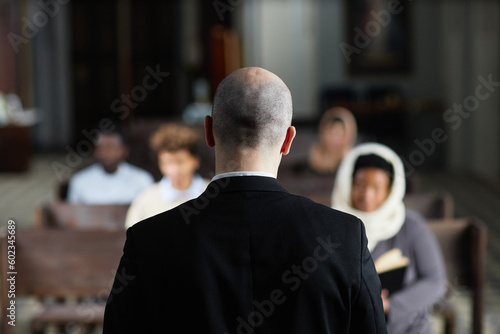 Rear view of pastor in black suit talking to believers while tehy sitting on bench in church
