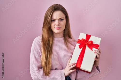 Young caucasian woman holding gift skeptic and nervous, frowning upset because of problem. negative person.