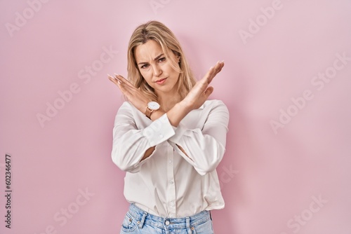 Young caucasian woman wearing casual white shirt over pink background rejection expression crossing arms doing negative sign  angry face