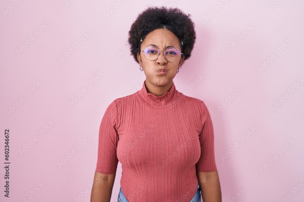 Beautiful african woman with curly hair standing over pink background puffing cheeks with funny face. mouth inflated with air, crazy expression. Beautiful african woman with curly hair standing over pink background puffing cheeks with funny face. mouth inflated with air, crazy expression.
