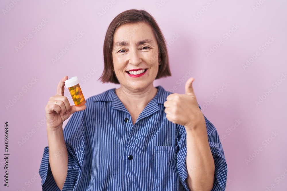 Middle age hispanic woman holding pills smiling happy and positive, thumb up doing excellent and approval sign Middle age hispanic woman holding pills smiling happy and positive, thumb up doing excellent and approval sign