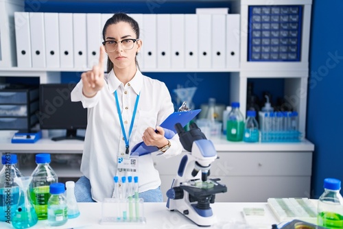Fototapeta Naklejka Na Ścianę i Meble -  Young brunette woman working at scientist laboratory pointing with finger up and angry expression, showing no gesture