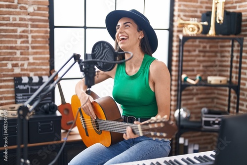 Young hispanic woman musician singing song playing classical guitar at music studio