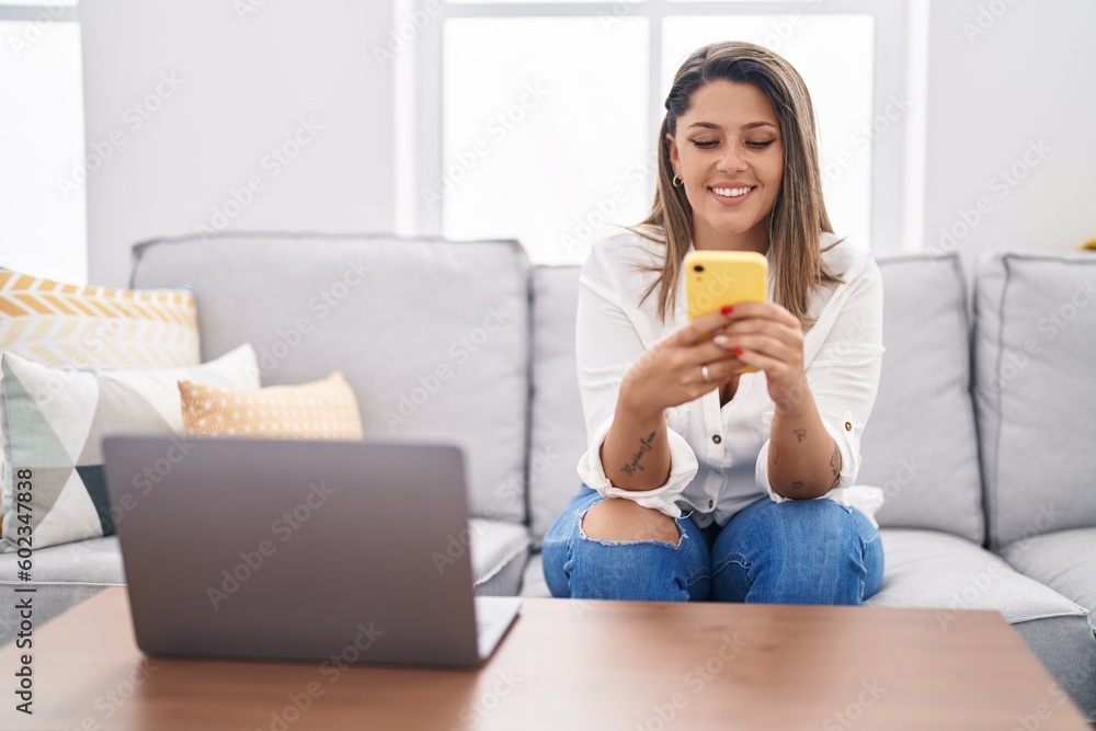 Young hispanic woman using smartphone sitting on sofa at home Young hispanic woman using smartphone sitting on sofa at home