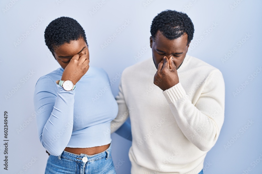 Young african american couple standing over blue background tired rubbing nose and eyes feeling fatigue and headache. stress and frustration concept. Young african american couple standing over blue background tired rubbing nose and eyes feeling fatigue and headache. stress and frustration concept.