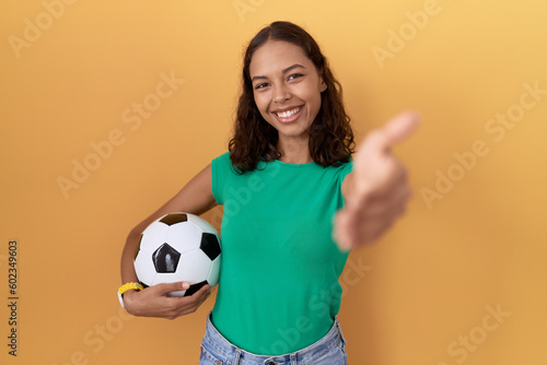 Young hispanic woman holding ball smiling friendly offering handshake as greeting and welcoming. successful business. © Krakenimages.com