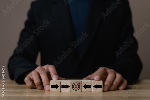 Business strategy. Businessman pointing wooden cube with target board icon and arrow on wooden desk. Goals and planning for success in marketing business, achieve the objective concept. free space