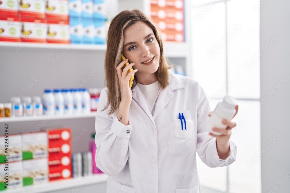Young woman pharmacist talking on smartphone holding pills at pharmacy