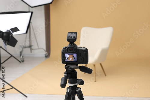 Camera on tripod, armchair and professional lighting equipment in modern photo studio
