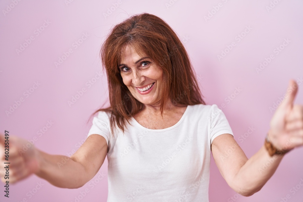 Middle age woman standing over pink background approving doing positive gesture with hand, thumbs up smiling and happy for success. winner gesture. Middle age woman standing over pink background approving doing positive gesture with hand, thumbs up smiling and happy for success. winner gesture.