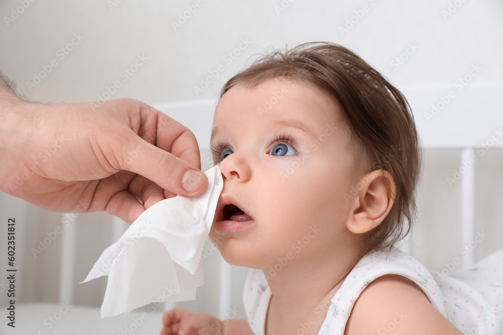 Father wiping runny nose of little baby with napkin on bed, closeup Father wiping runny nose of little baby with napkin on bed, closeup
