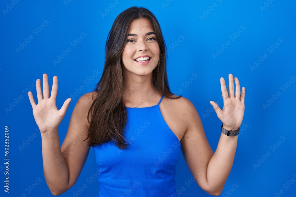 Hispanic woman standing over blue background showing and pointing up with fingers number ten while smiling confident and happy. Hispanic woman standing over blue background showing and pointing up with fingers number ten while smiling confident and happy.