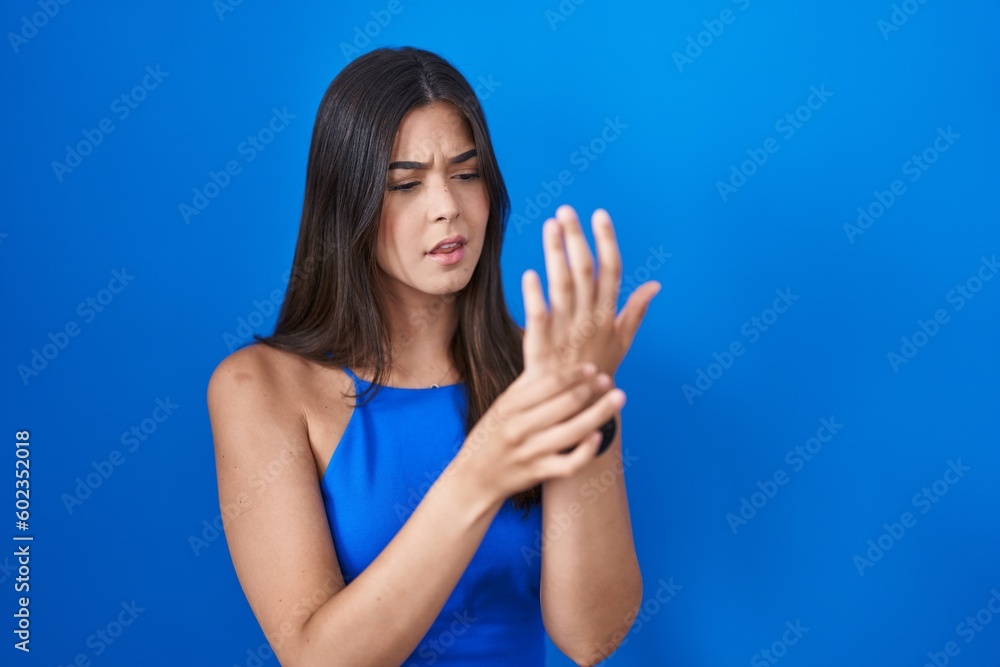 Hispanic woman standing over blue background suffering pain on hands and fingers, arthritis inflammation Hispanic woman standing over blue background suffering pain on hands and fingers, arthritis inflammation