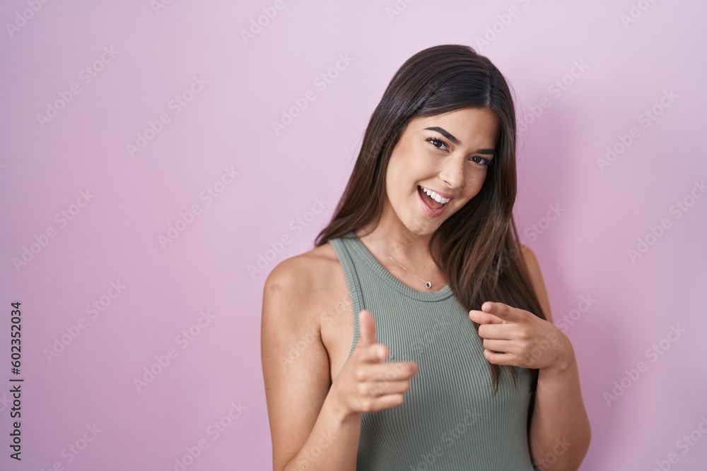 Hispanic woman standing over pink background pointing fingers to camera with happy and funny face. good energy and vibes. Hispanic woman standing over pink background pointing fingers to camera with happy and funny face. good energy and vibes.
