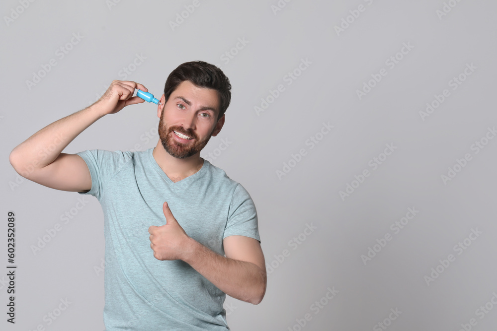 Man using ear drops and showing thumbs up on grey background, space for text Man using ear drops and showing thumbs up on grey background, space for text