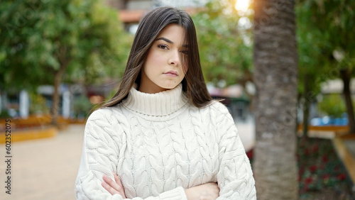 Young beautiful hispanic woman standing with serious expression and arms crossed gesture at park