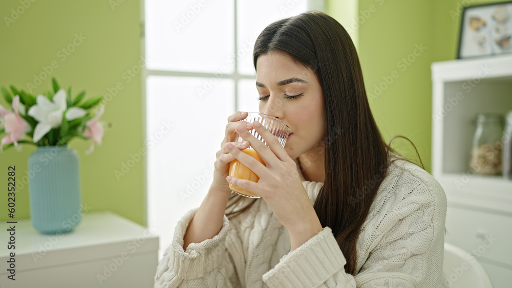 Young beautiful hispanic woman drinking orange juice sitting on table at home Young beautiful hispanic woman drinking orange juice sitting on table at home