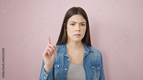 Fotografie Young beautiful hispanic woman saying no with finger over isolated pink backgrou