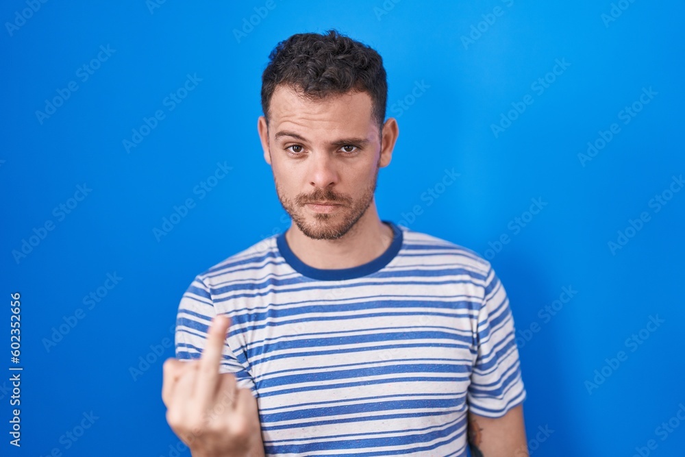 Young hispanic man standing over blue background showing middle finger, impolite and rude fuck off expression Young hispanic man standing over blue background showing middle finger, impolite and rude fuck off expression