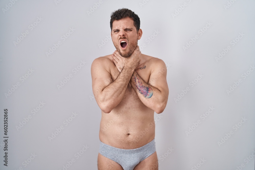 Young hispanic man standing shirtless wearing underware shouting suffocate because painful strangle. health problem. asphyxiate and suicide concept.