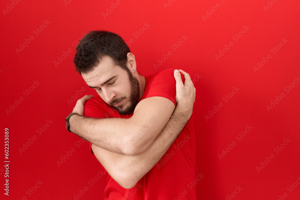 Young hispanic man wearing casual red t shirt hugging oneself happy and positive, smiling confident. self love and self care Young hispanic man wearing casual red t shirt hugging oneself happy and positive, smiling confident. self love and self care