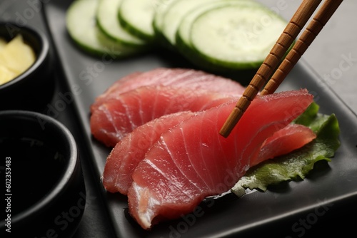 Taking tasty sashimi (piece of fresh raw tuna) from black plate at table, closeup