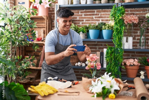 Young hispanic man florist make photo to plant by smartphone at flower shop