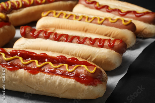 Fresh delicious hot dogs with sauces on black table, closeup