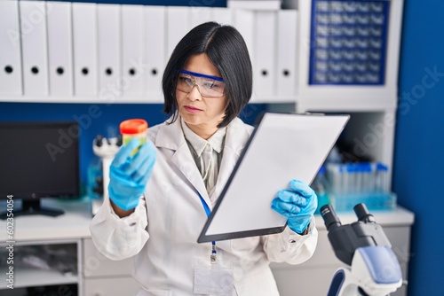 Young chinese woman scientist analysing urine reading report document at laboratory