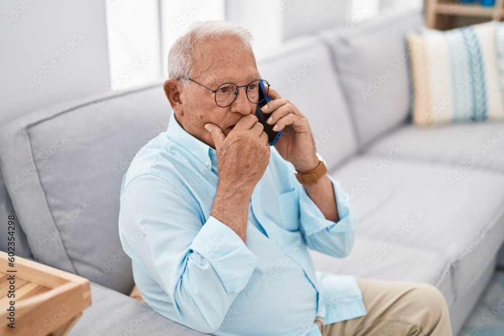 Senior grey-haired man talking on smartphone sitting on sofa at home Senior grey-haired man talking on smartphone sitting on sofa at home