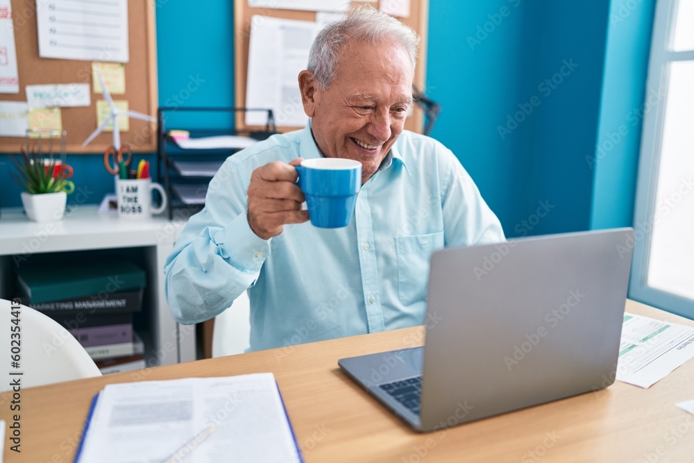 Middle age grey-haired man business worker using laptop drinking coffee at office Middle age grey-haired man business worker using laptop drinking coffee at office