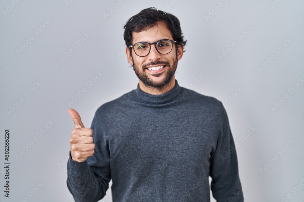 Fototapeta premium Handsome latin man standing over isolated background doing happy thumbs up gesture with hand. approving expression looking at the camera showing success.