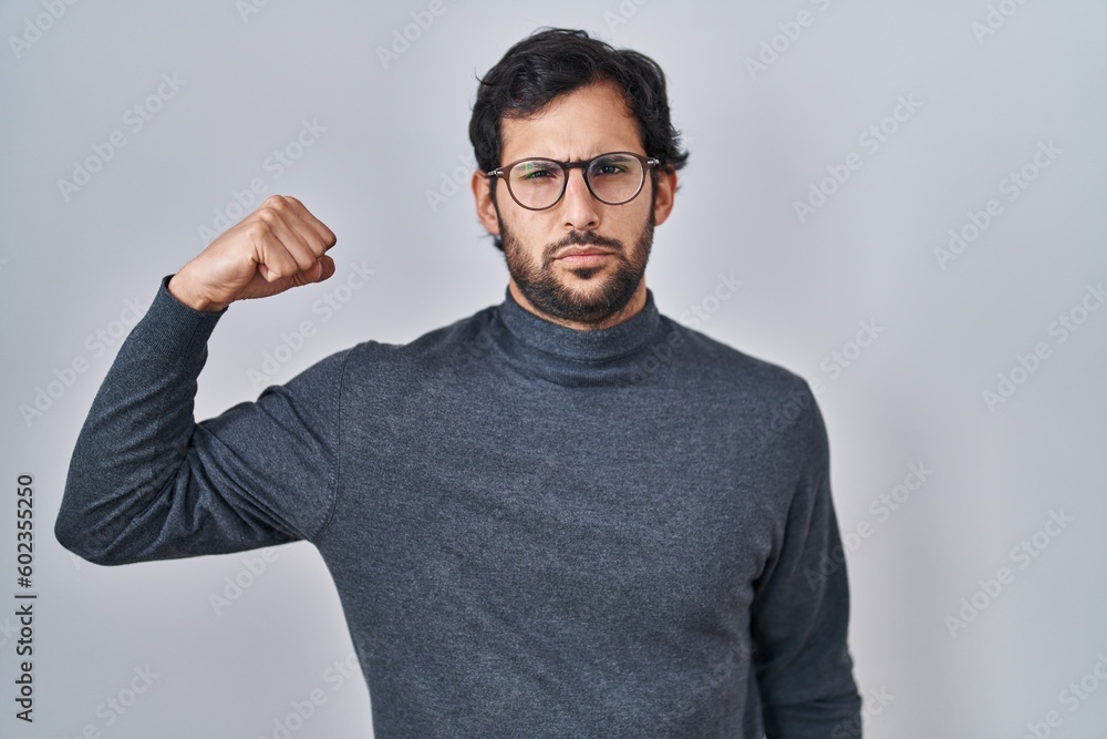 Handsome latin man standing over isolated background strong person showing arm muscle, confident and proud of power Handsome latin man standing over isolated background strong person showing arm muscle, confident and proud of power