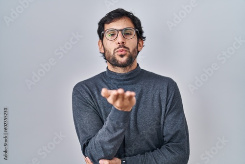 Handsome latin man standing over isolated background looking at the camera blowing a kiss with hand on air being lovely and sexy. love expression.