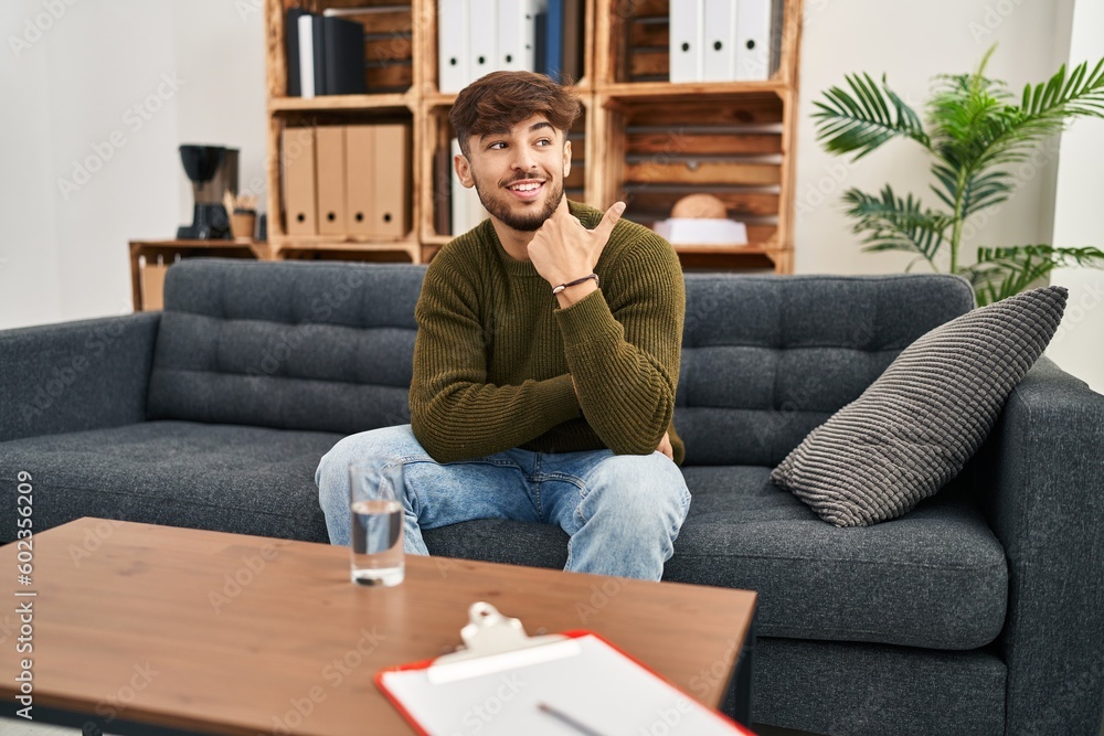 Arab man with beard working on depression at therapy office pointing thumb up to the side smiling happy with open mouth Arab man with beard working on depression at therapy office pointing thumb up to the side smiling happy with open mouth