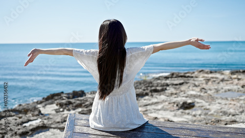 Obraz na plátně Young chinese woman sitting on bench with arms open at seaside