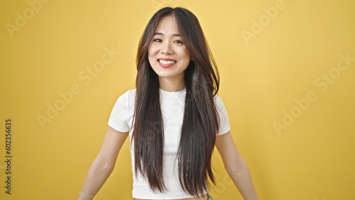 Obraz na plátně Young chinese woman smiling confident standing over isolated yellow background