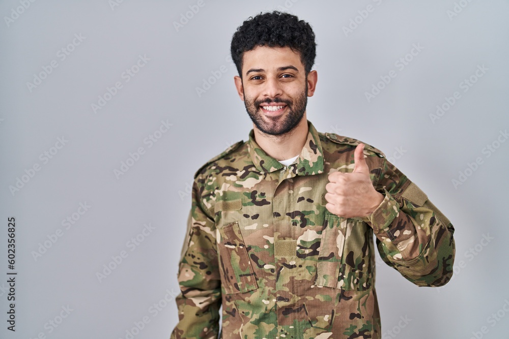 Arab man wearing camouflage army uniform doing happy thumbs up gesture with hand. approving expression looking at the camera showing success. Arab man wearing camouflage army uniform doing happy thumbs up gesture with hand. approving expression looking at the camera showing success.