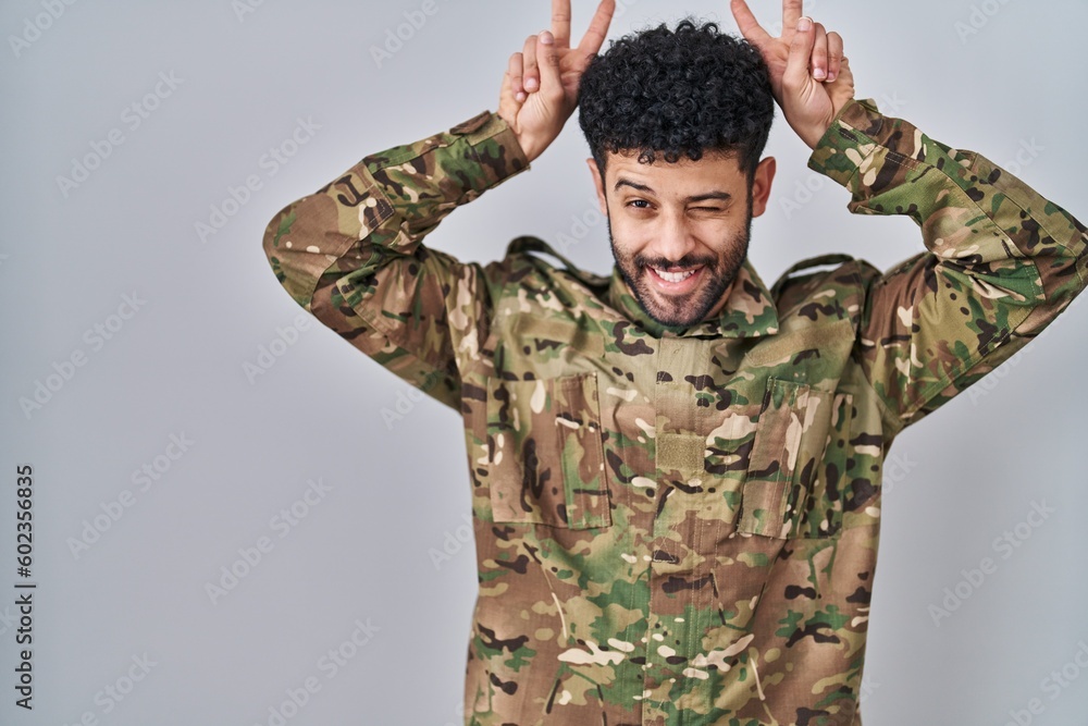 Arab man wearing camouflage army uniform posing funny and crazy with fingers on head as bunny ears, smiling cheerful Arab man wearing camouflage army uniform posing funny and crazy with fingers on head as bunny ears, smiling cheerful