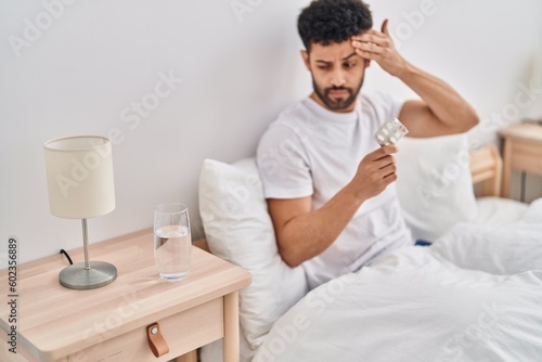 Young arab man taking pills for headache sitting on bed at bedroom