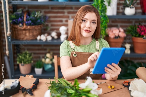 Young redhead woman florist smiling confident using touchpad at flower shop