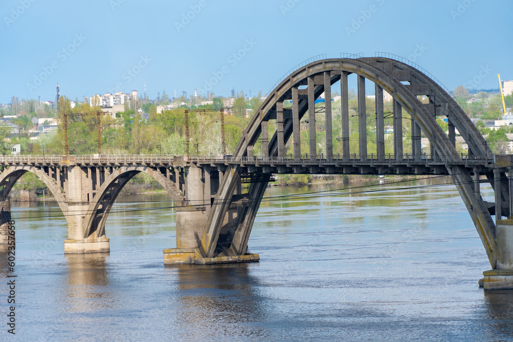 View of river Dnepr and railway ancient arched bridge. Unique construction across wide water 19th century. Railway line along the Merefo-Kherson bridge. Panoramic on modern city and spring landscape. View of river Dnepr and railway ancient arched bridge. Unique construction across wide water 19th century. Railway line along the Merefo-Kherson bridge. Panoramic on modern city and spring landscape.