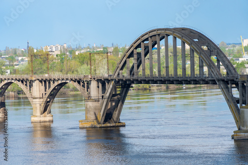 View of river Dnepr and railway ancient arched bridge. Unique construction across wide water 19th century. Railway line along the Merefo-Kherson bridge. Panoramic on modern city and spring landscape. © IhorStore