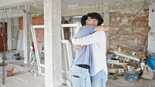 Two men couple smiling confident hugging each other at construction site