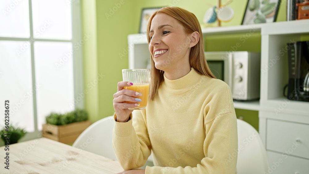 Young blonde woman drinking orange juice sitting on table at home Young blonde woman drinking orange juice sitting on table at home
