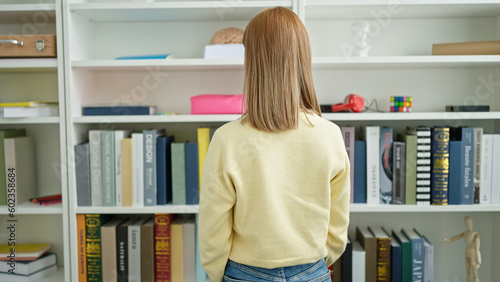 Young blonde woman student looking for book at university classroom