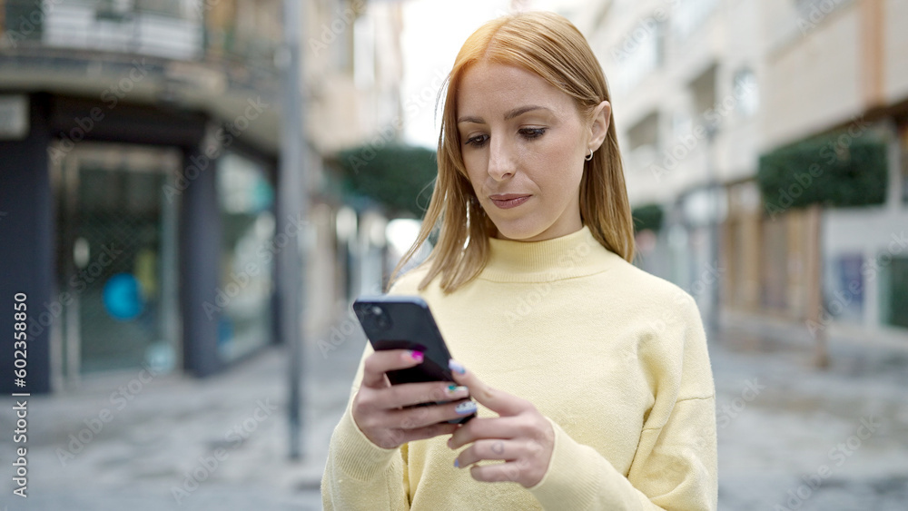 Young blonde woman using smartphone with serious expression at street