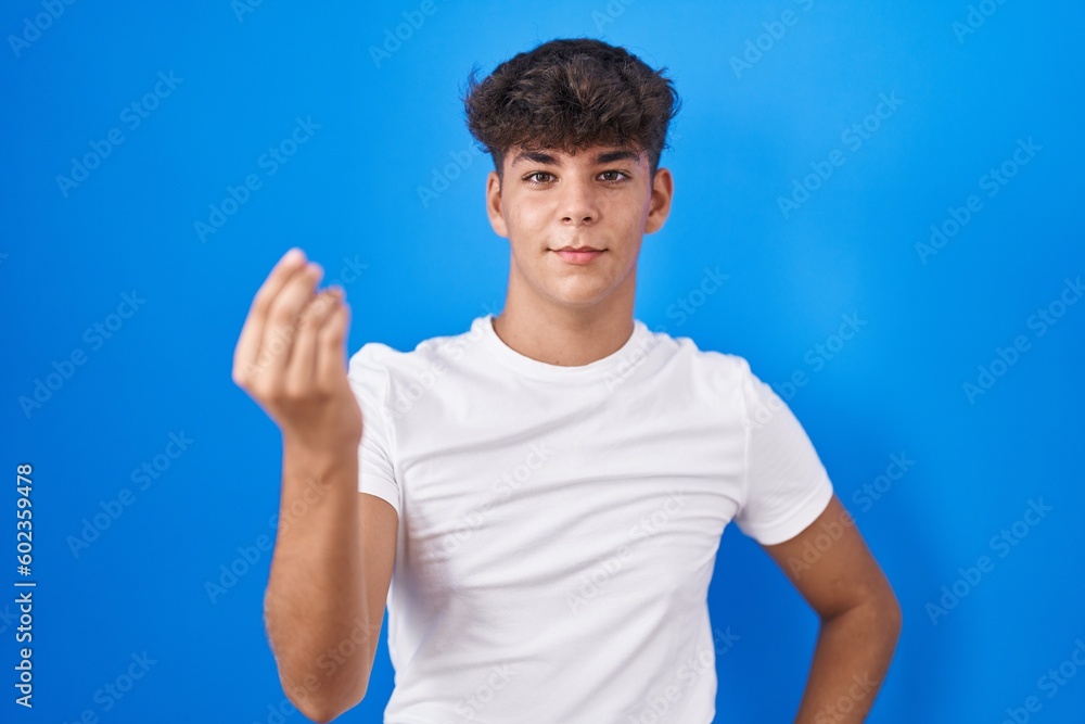 Hispanic teenager standing over blue background doing italian gesture with hand and fingers confident expression Hispanic teenager standing over blue background doing italian gesture with hand and fingers confident expression