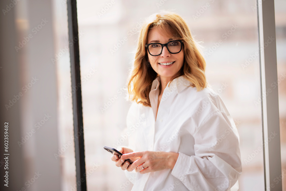 Confident woman standing in a modern office and using smartphone Confident woman standing in a modern office and using smartphone