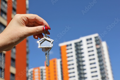 Real estate agent, home keys in female hand on background of new building. Byung apartment or renting property